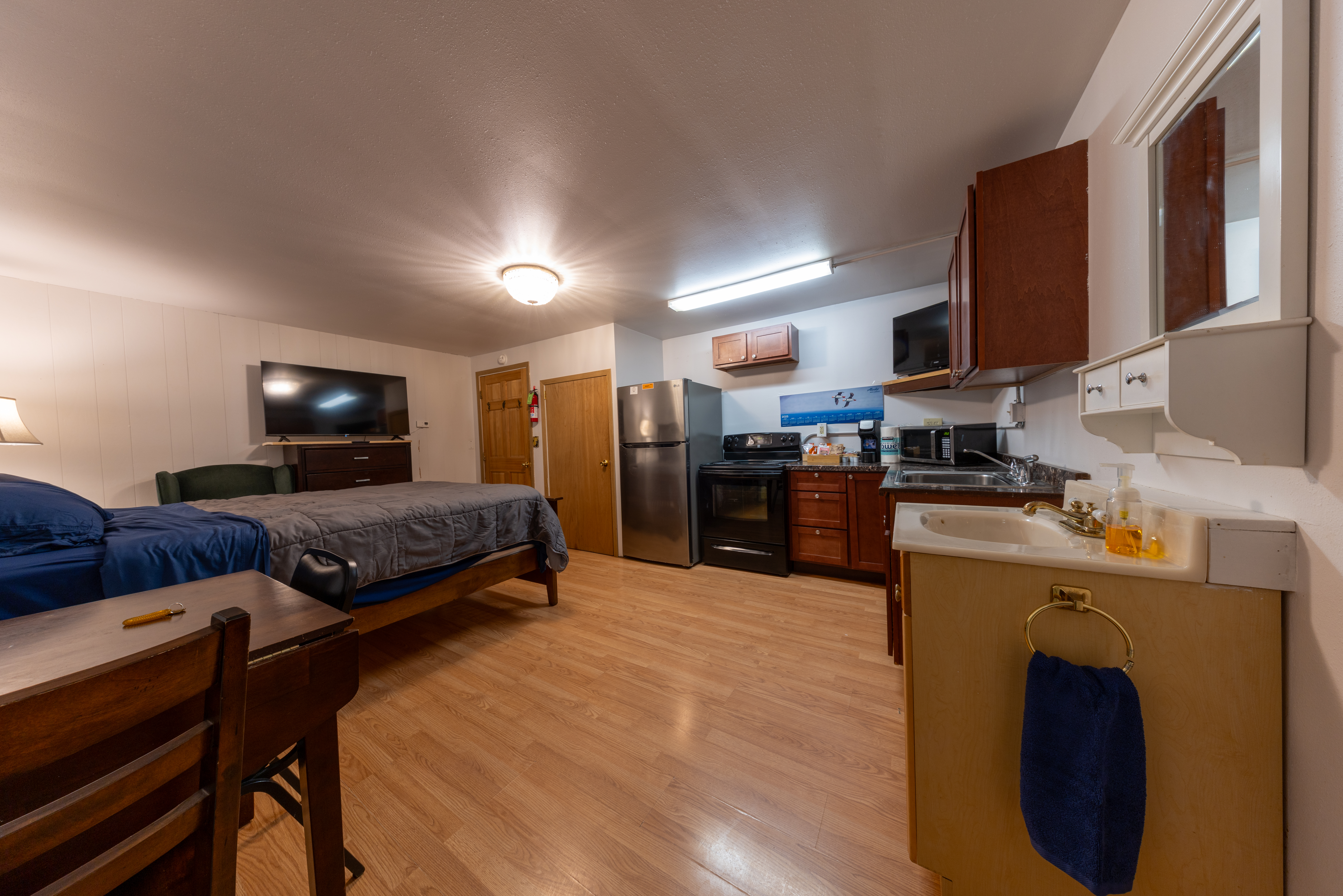 Studio room with bed, TV, and small kitchen area with fridge, stove, microwave, and sink