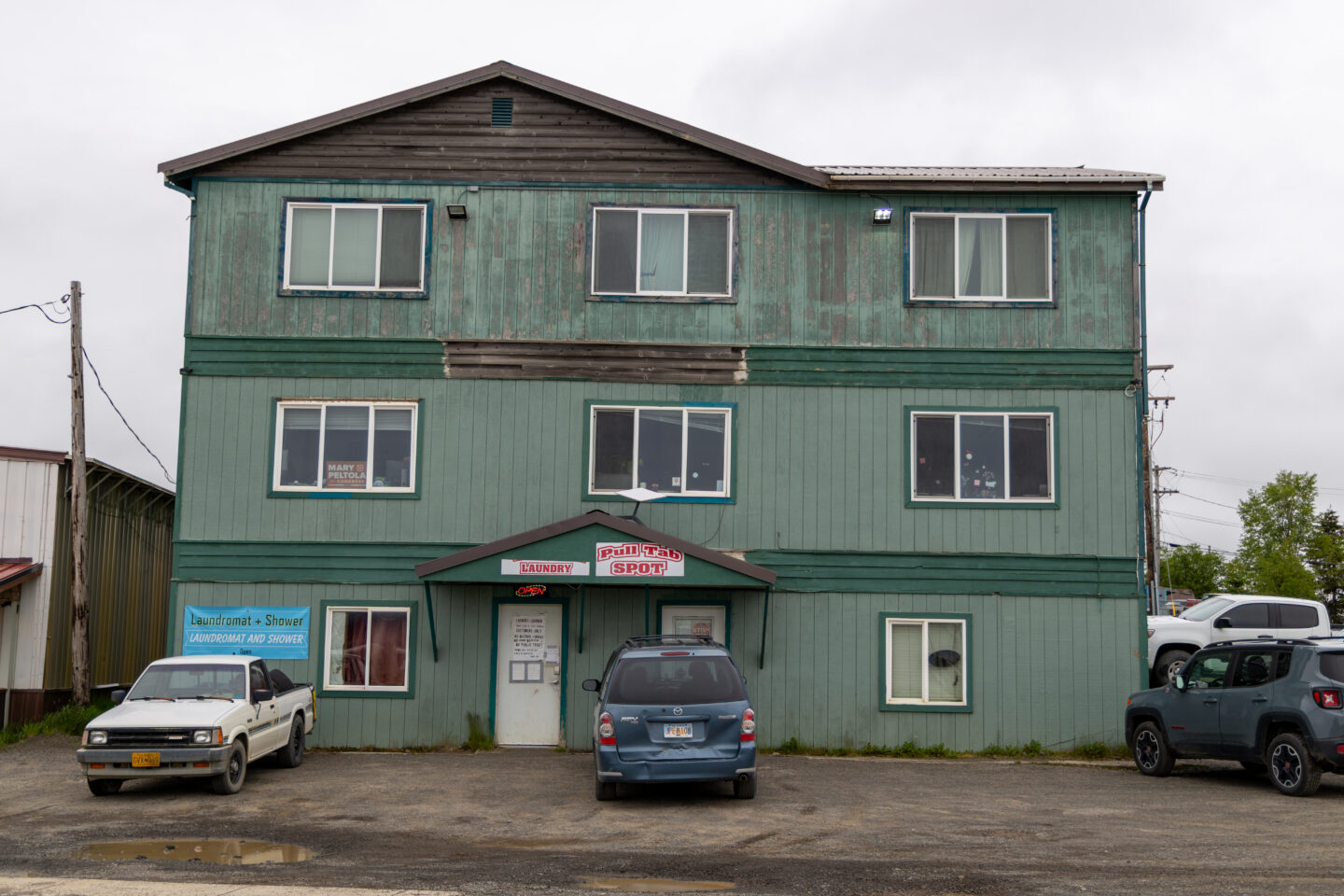 Three-story green building with laundromat and shower entrance on ground floor, cars parked in front