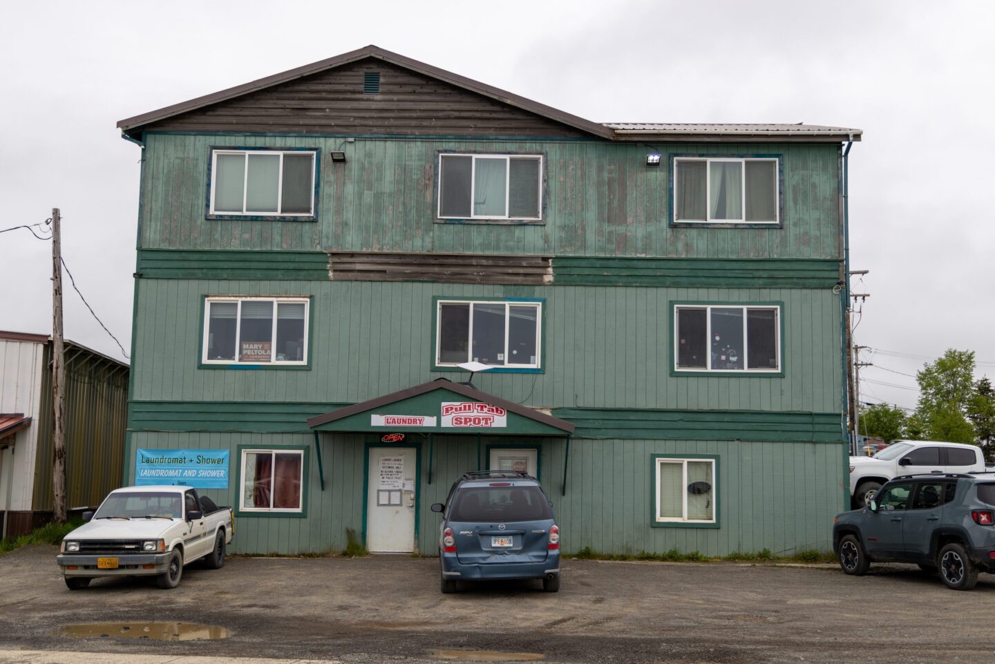 Three-story green building with laundromat and shower entrance on ground floor, cars parked in front