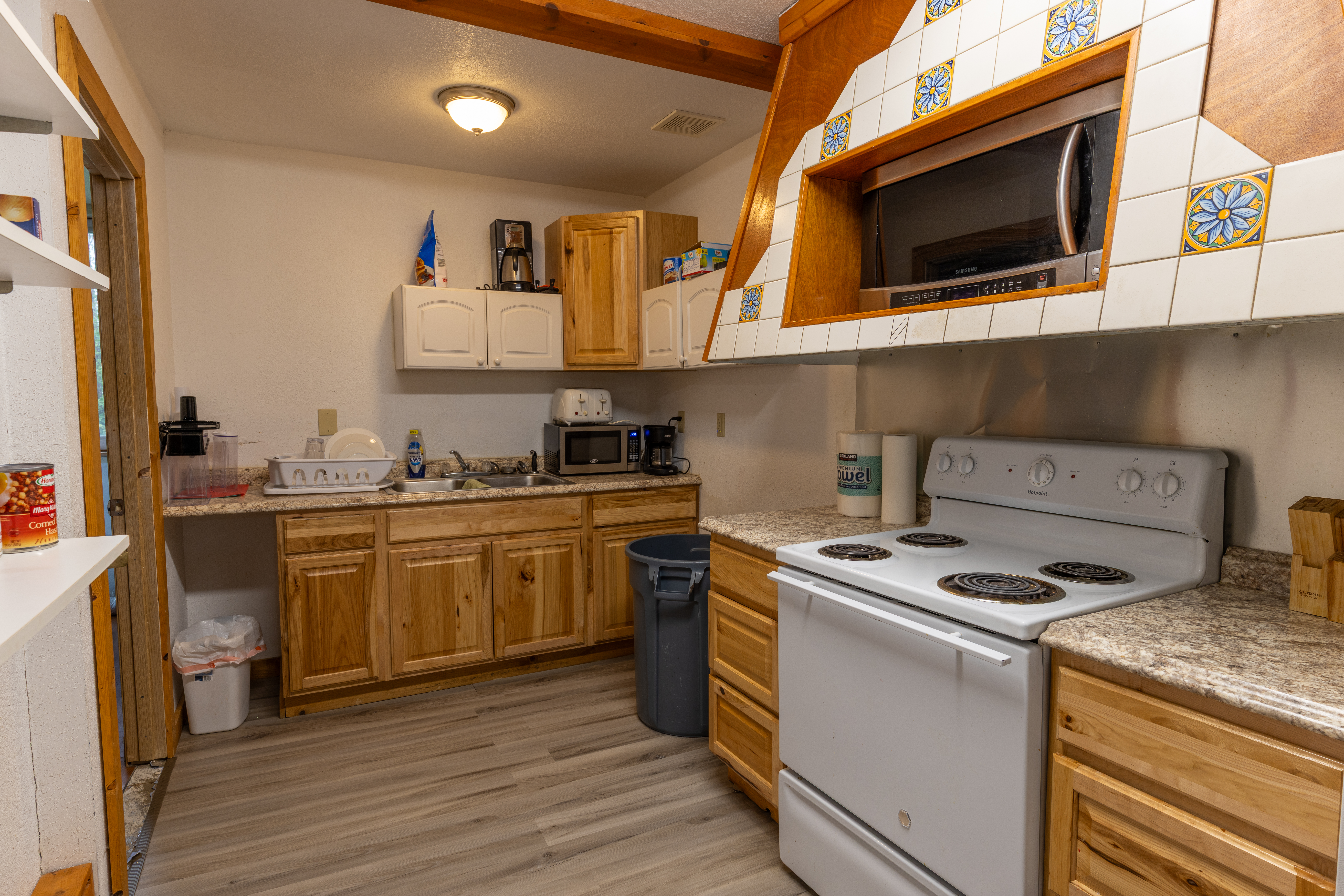 Kitchen with wood cabinets, white stove, microwave, and sink, featuring tiled hood and gray flooring