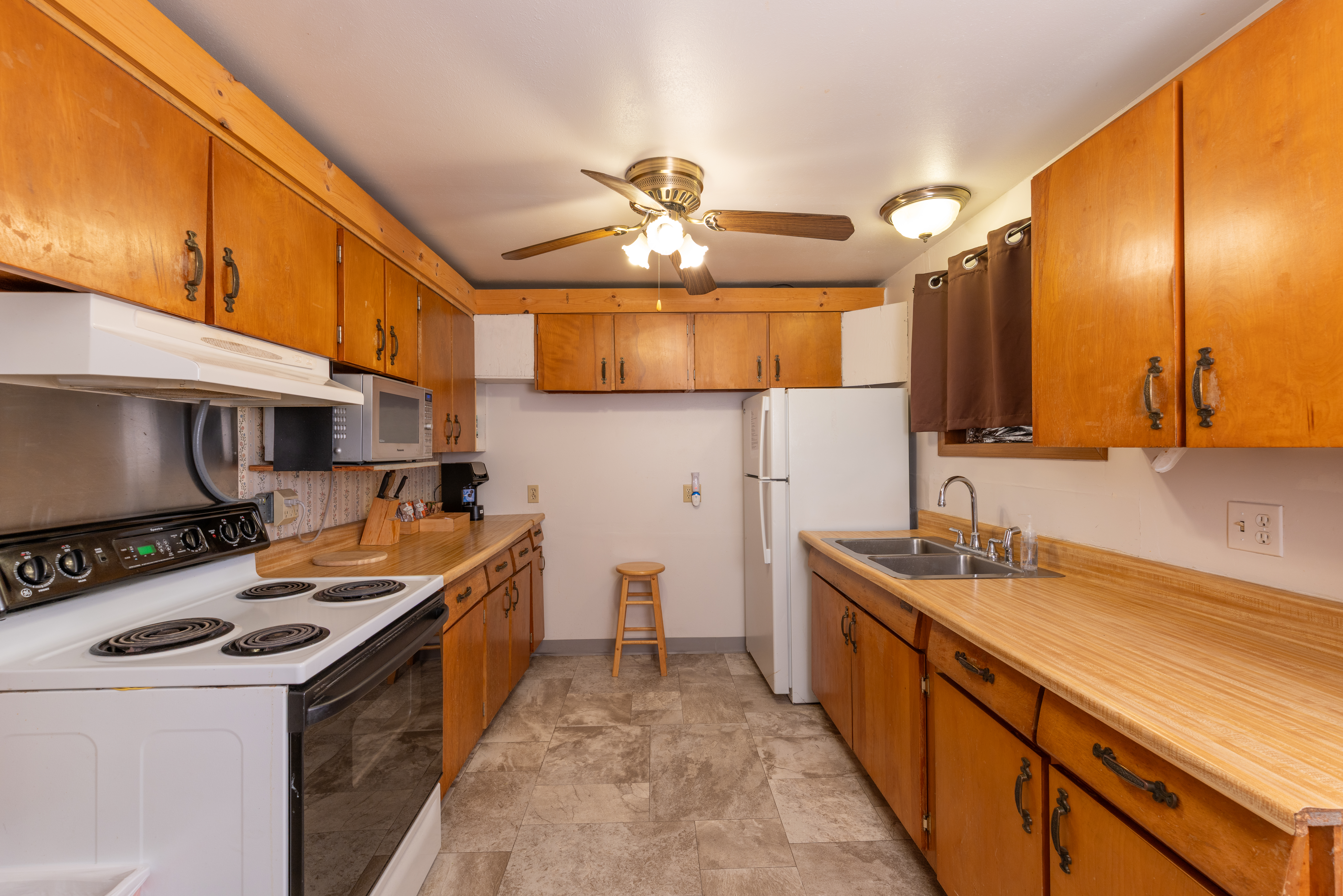 Retro-style kitchen with wood cabinets, white appliances, double sink, and ceiling fan lighting