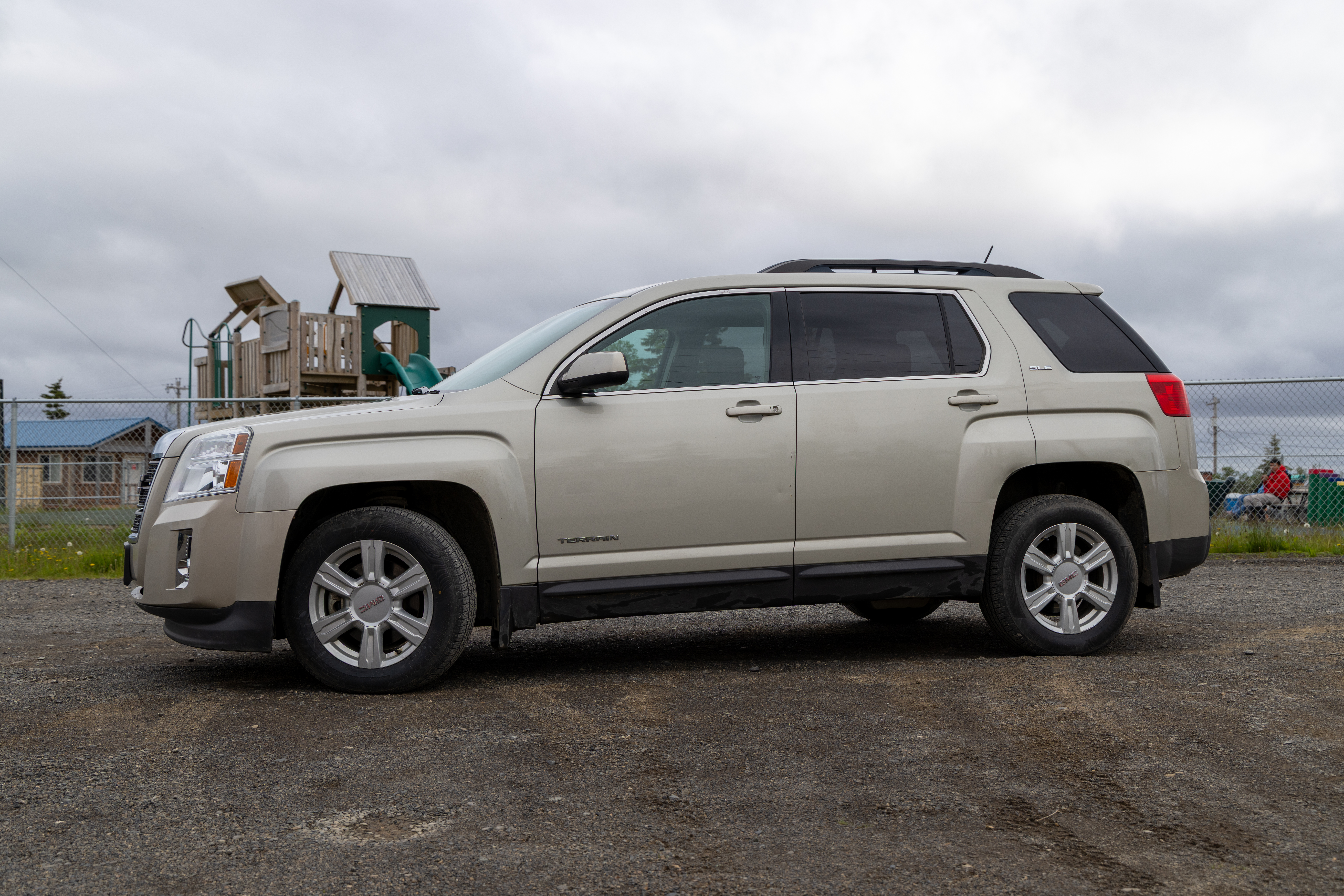 Beige GMC Terrain SUV parked on gravel lot near a playground