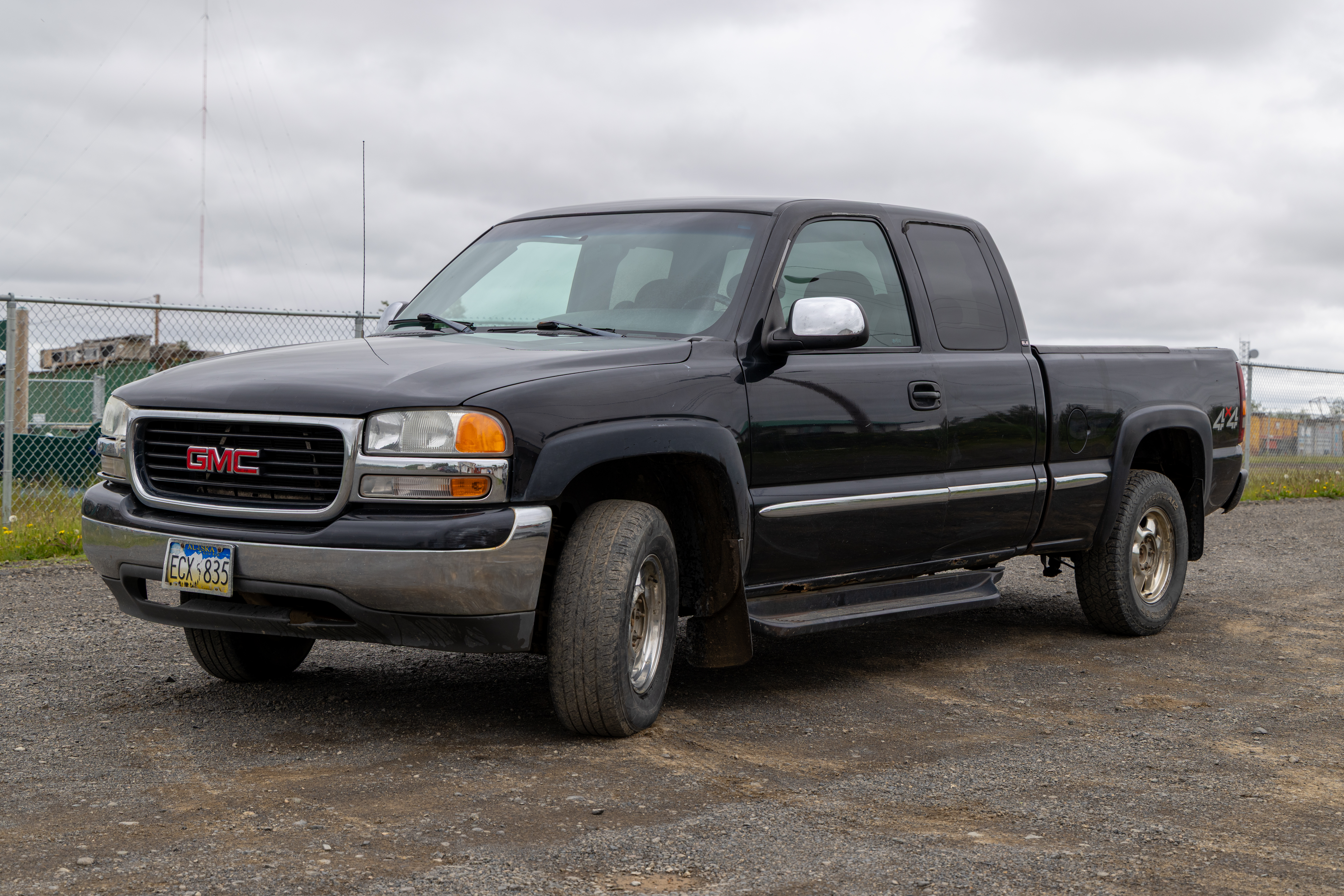 Black GMC pickup truck parked on gravel lot with cloudy sky background