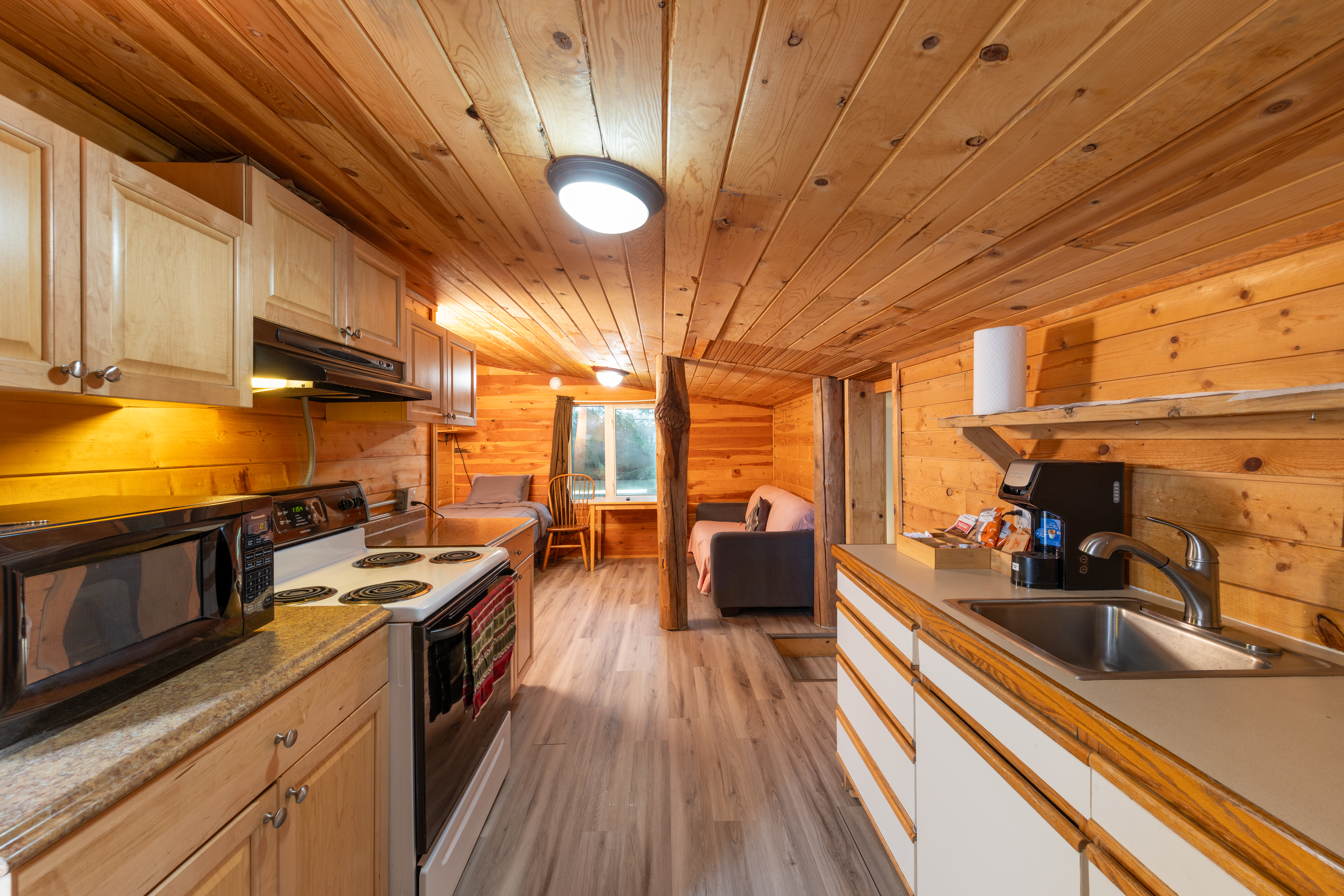 Cabin-style kitchen with wood walls and ceiling, stove, sink, and cozy seating area near window